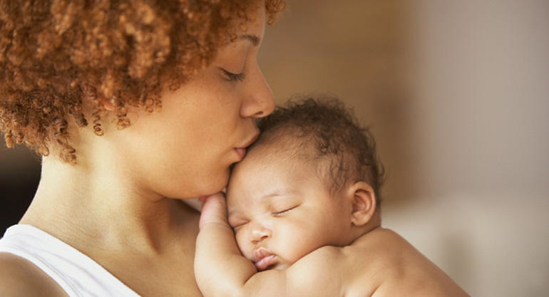 mother holding and kissing the forehead of sleeping baby