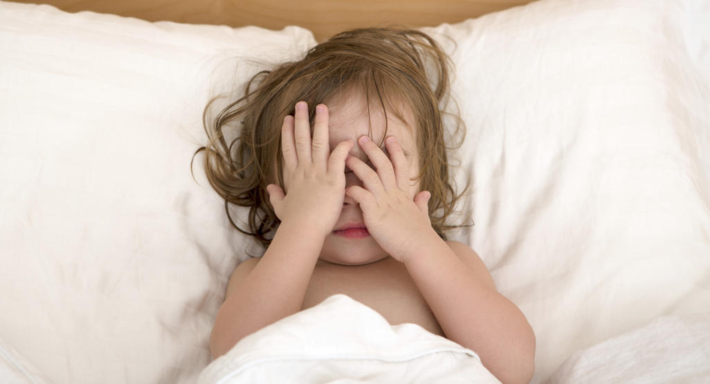 child lying in bed while covering her eyes with her hands