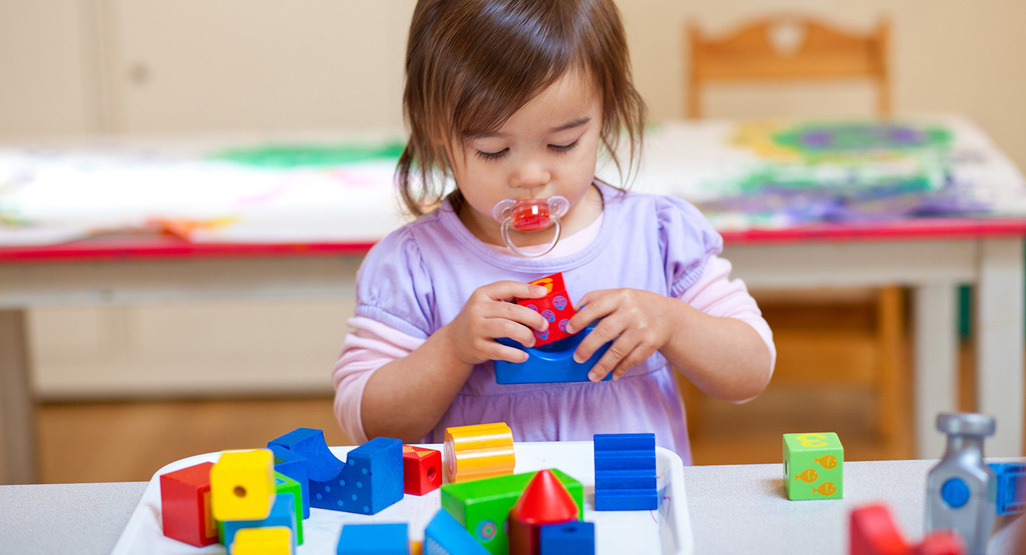 young child with pacifier in mouth playing with blocks