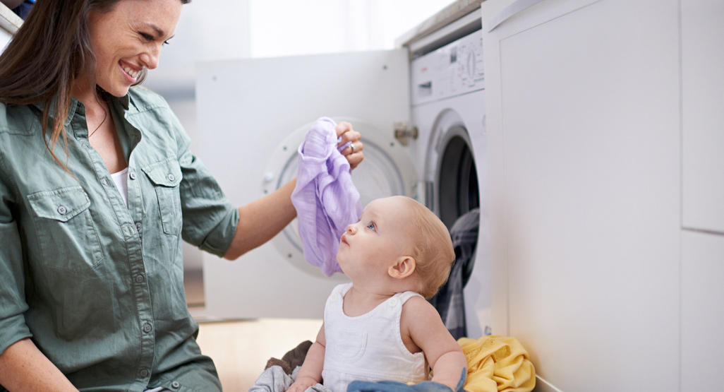 mom having fun with her baby while doing laundry