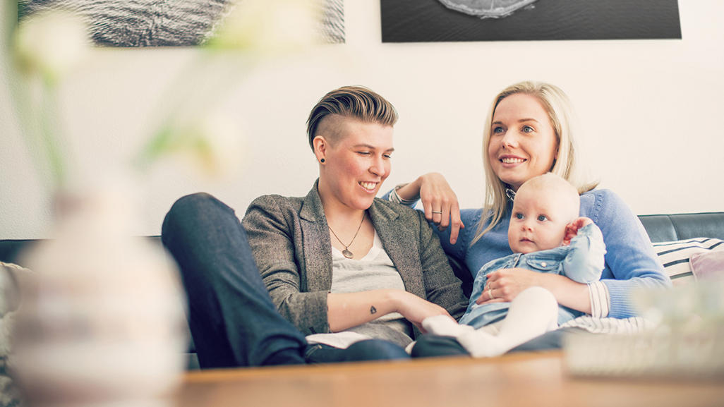 two women sitting on a couch and one of them holding baby on her lap
