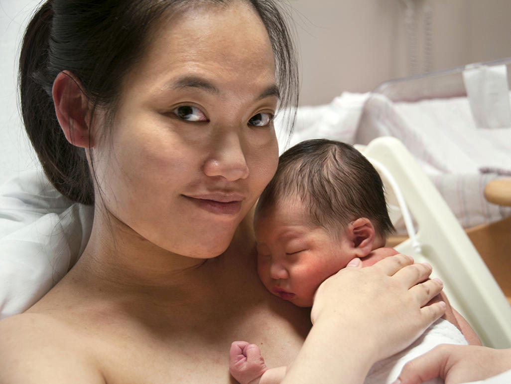 mother holding her newborn baby while lying on a bed