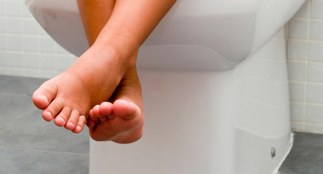 close up of child's legs while sitting on the toilet
