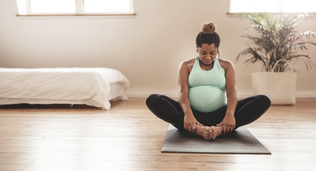 pregnant woman sitting on the yoga mat, stretching out