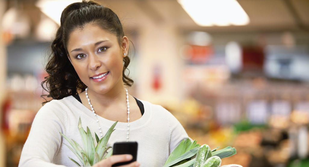 woman at a grocery store with greens and a phone in her hands