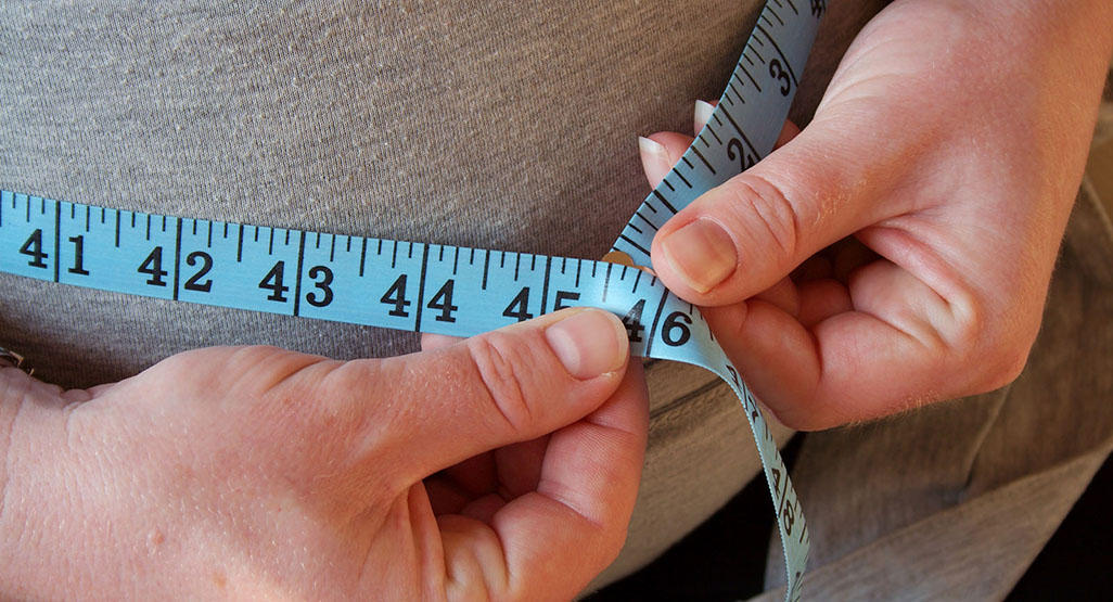 pregnant woman measuring her belly with a measuring tape