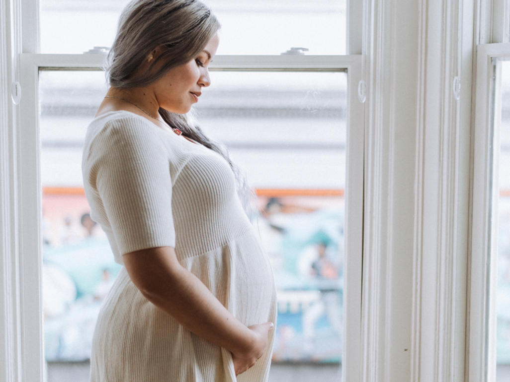 profile photo of a woman holding her pregnant belly in her hands in front of a window