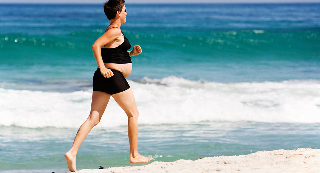 pregnant woman running on a beach