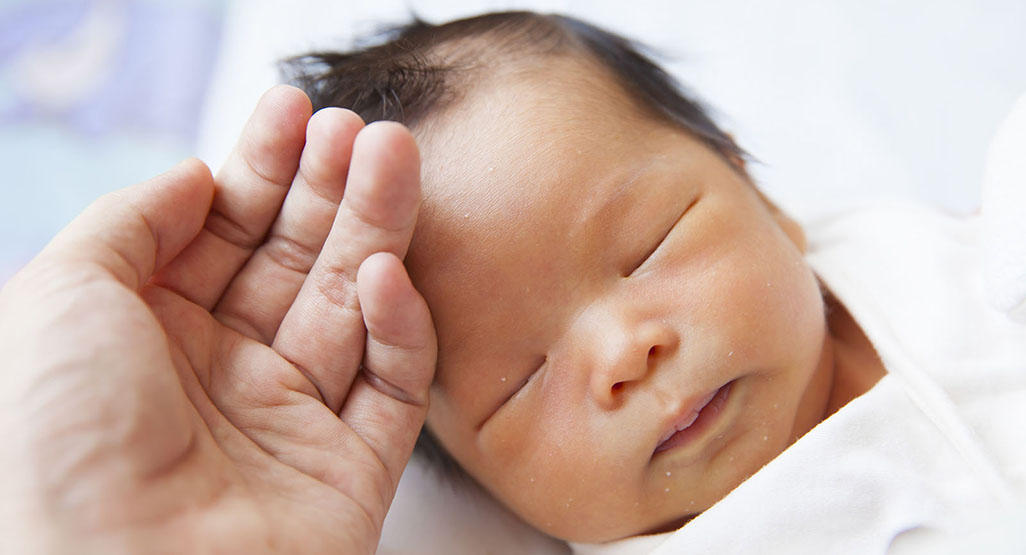 hand cuddling newborn baby's forehead
