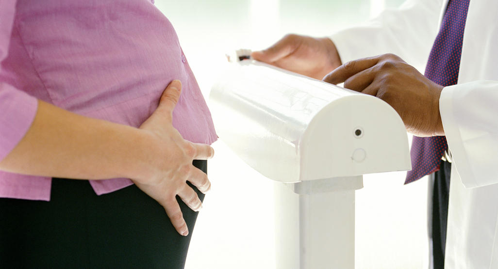 pregnant woman getting weighed by a doctor