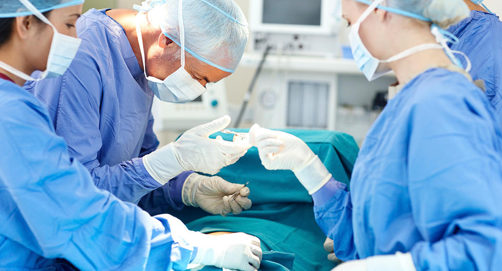 three doctors in operating room holding medical instruments while performing a surgery