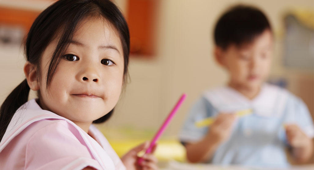 preschooler girl sitting at a desk holding a pen