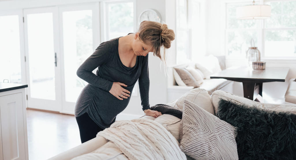 pregnant woman leaning over a couch holding her pregnant belly
