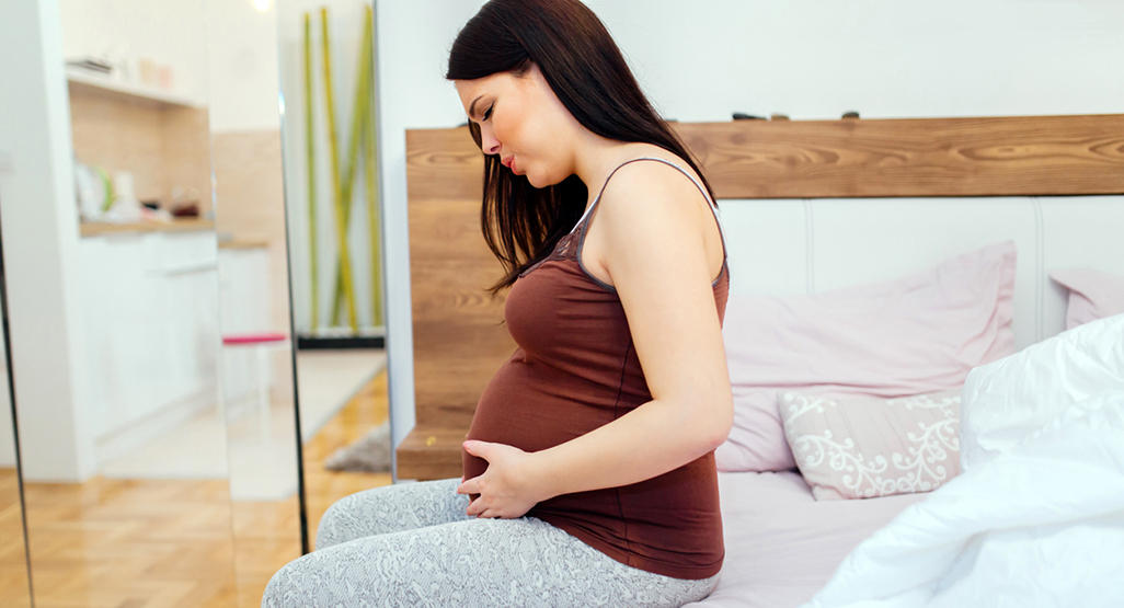 pregnant woman sitting on the bed while making pained facial expression and body posture