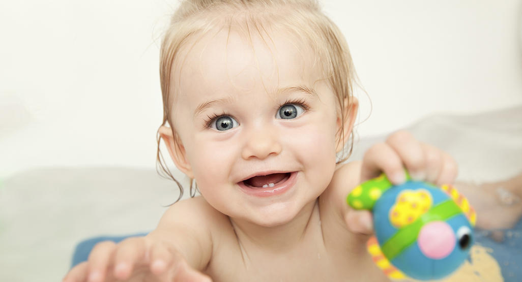 baby with blond hair and blue eyes bathing and holding a toy fish