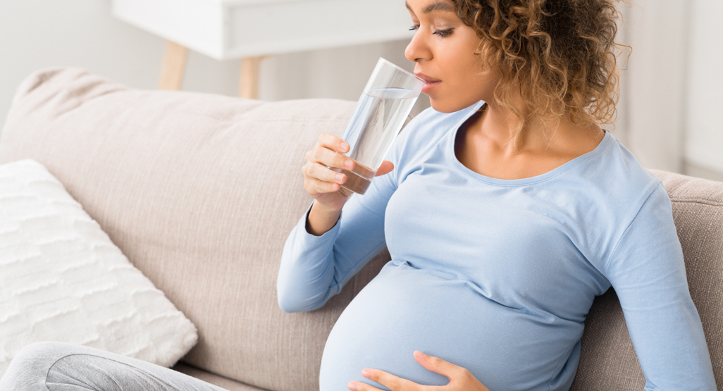 pregnant woman sitting on couch drinking water