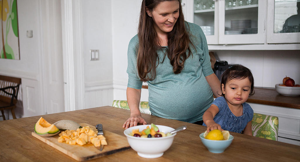 pregnant woman teaching her child to eat fruits from the kitchen counter