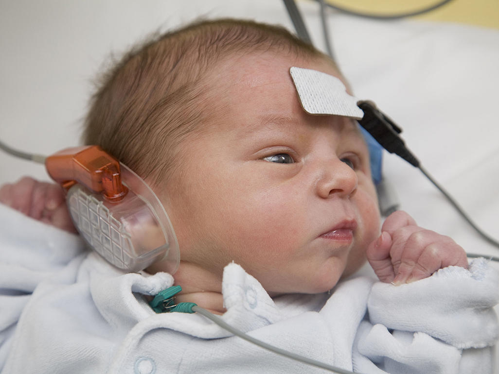 newborn with device around ear and pad with wire on forehead