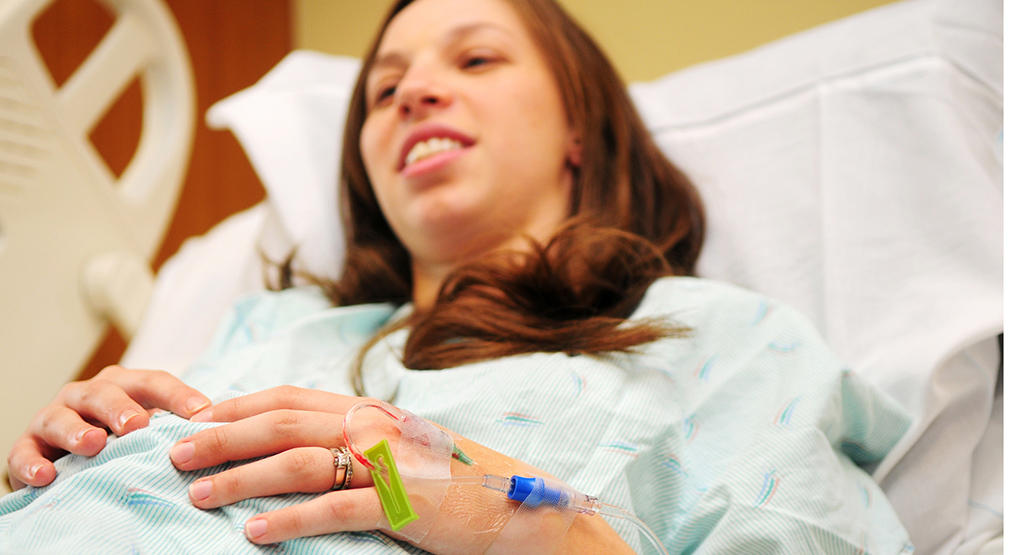 pregnant woman laying on a hospital bed with I.V. needle attached to her hand