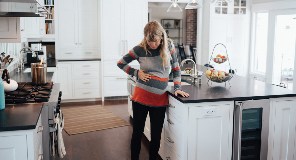 pregnant woman clasping her hands on her belly as if she is cramping