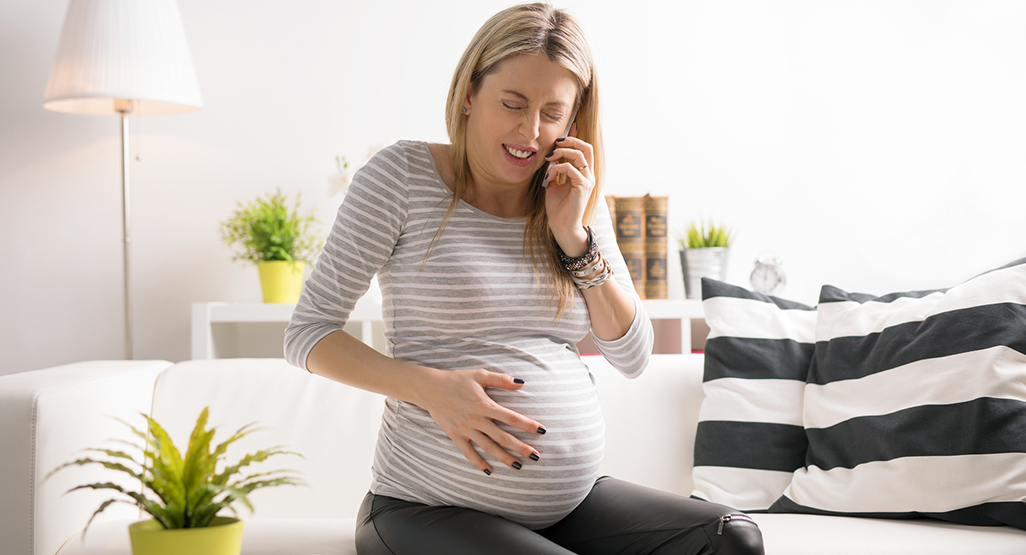 woman clutching her pregnant belly as if she's in pain while making a phone call