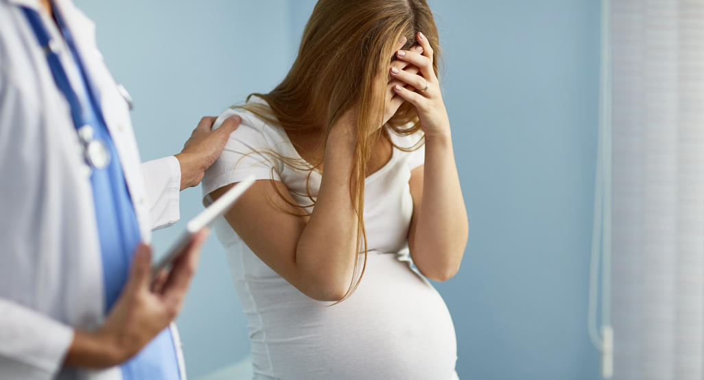 pregnant woman holding her head in despair, while the doctor is trying to comfort her