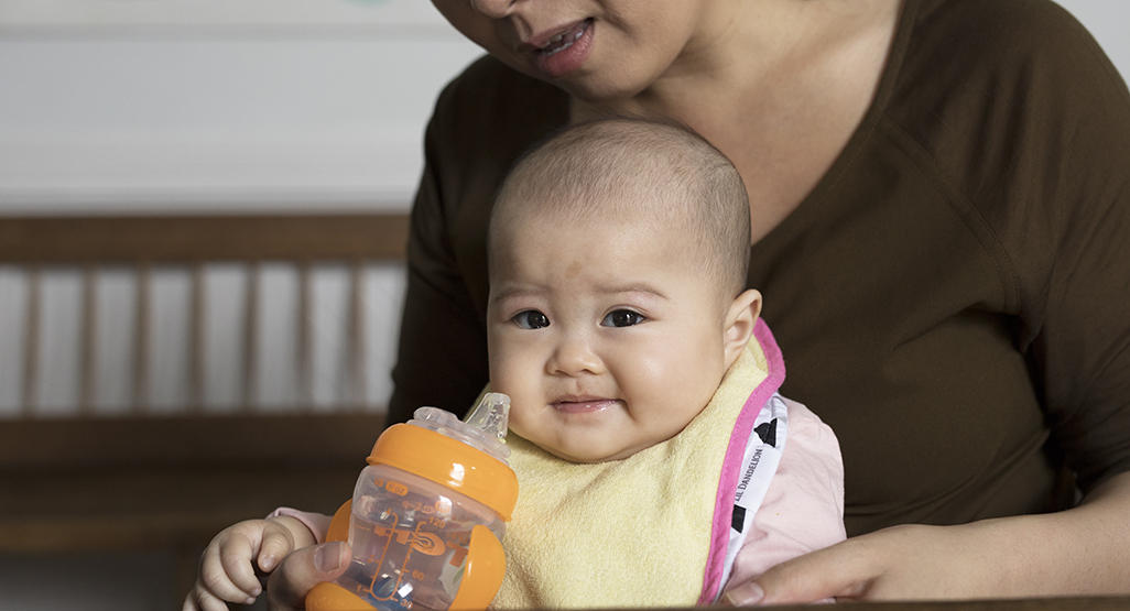 Infant on mom's lap drinking water from the sippy cup