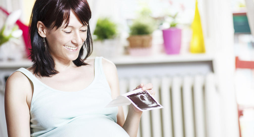 pregnant woman holding a picture of her ultrasound laughing