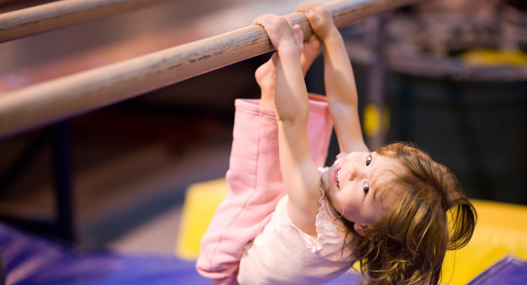 girl hanging from gymnastics bar in toes to the bar position