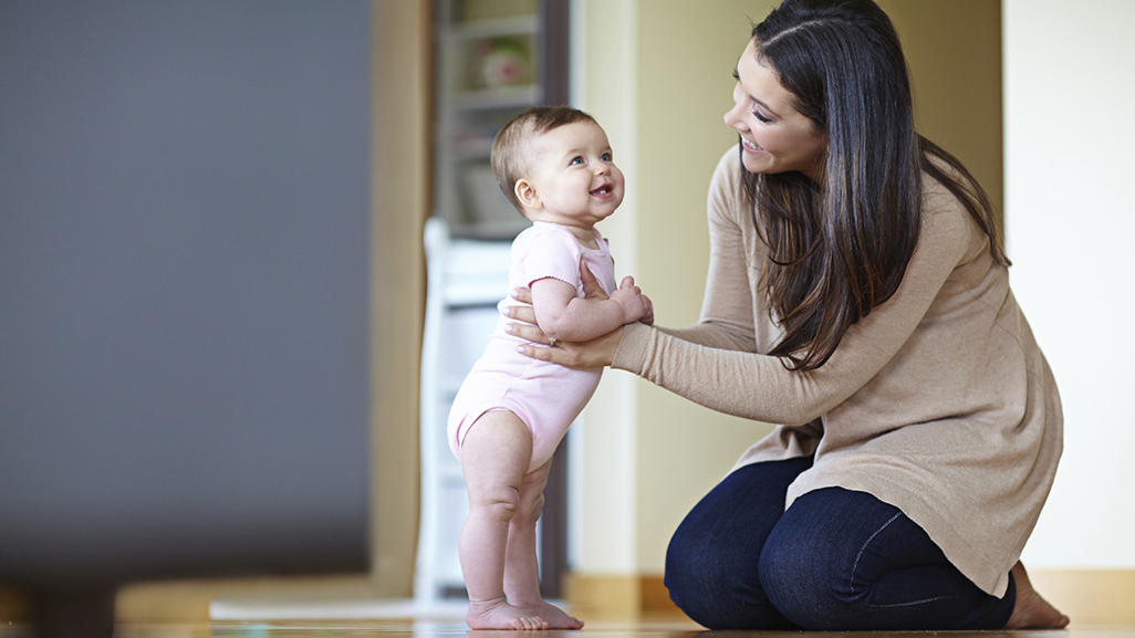 happy woman kneeling on a floor and teaching smiling baby to walk