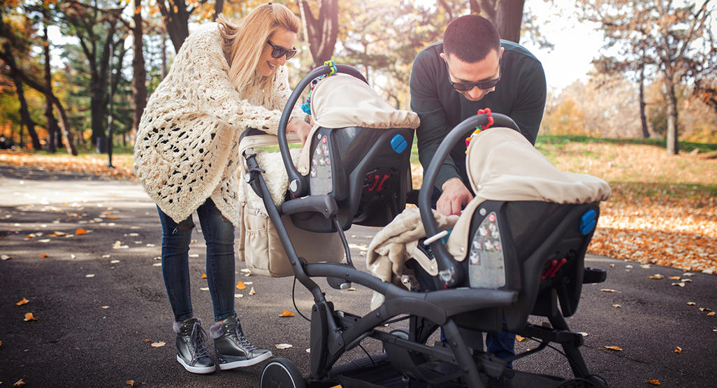 couple with double stroller taking care of each child separately at the same time while staying at the park
